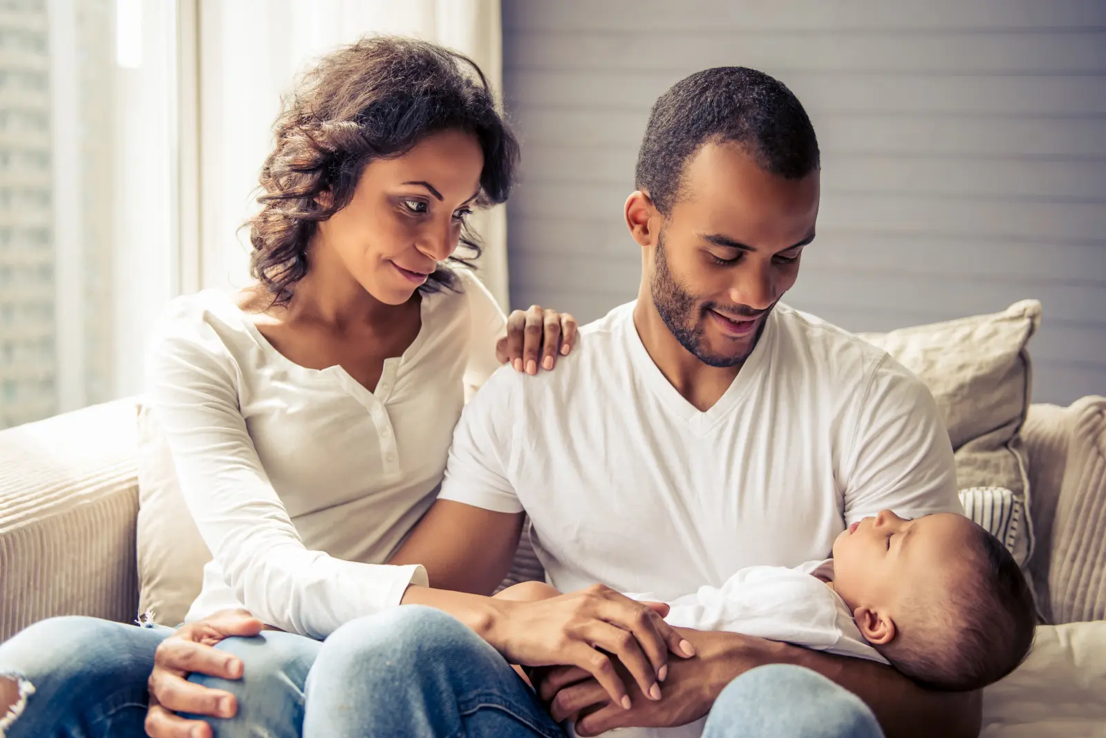Parents on a sofa gazing at their sleeping newborn