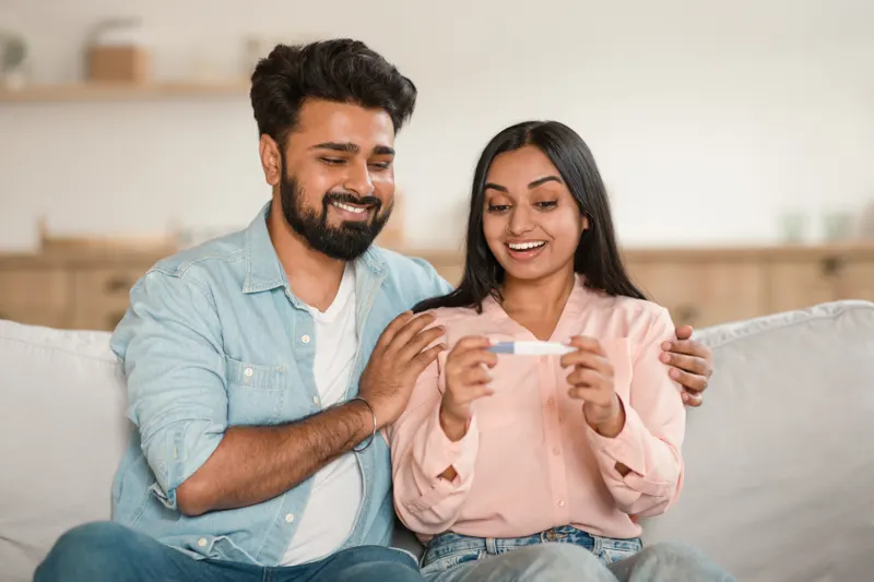 A happy couple on their sofa looking at a positive pregnancy test together