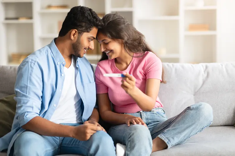 A young couple smiling together over a positive pregnancy test