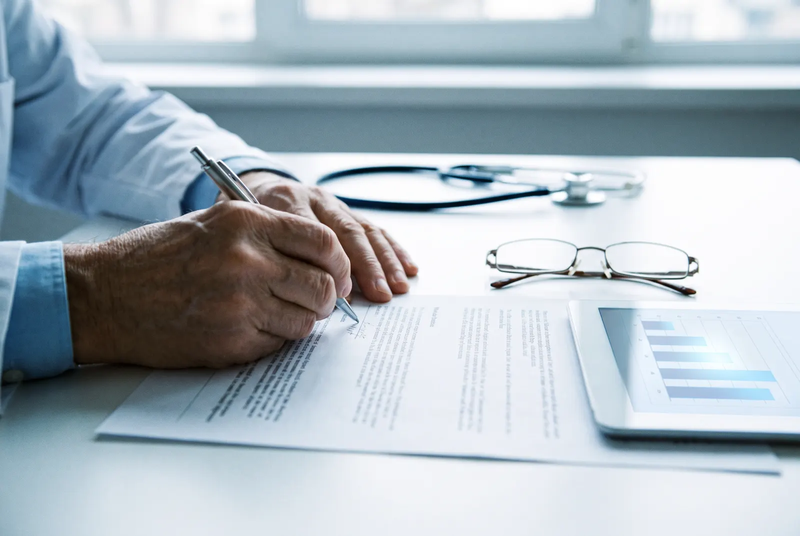 A senior doctor making handwritten notes on a printed clinical protocol beside a tablet chart