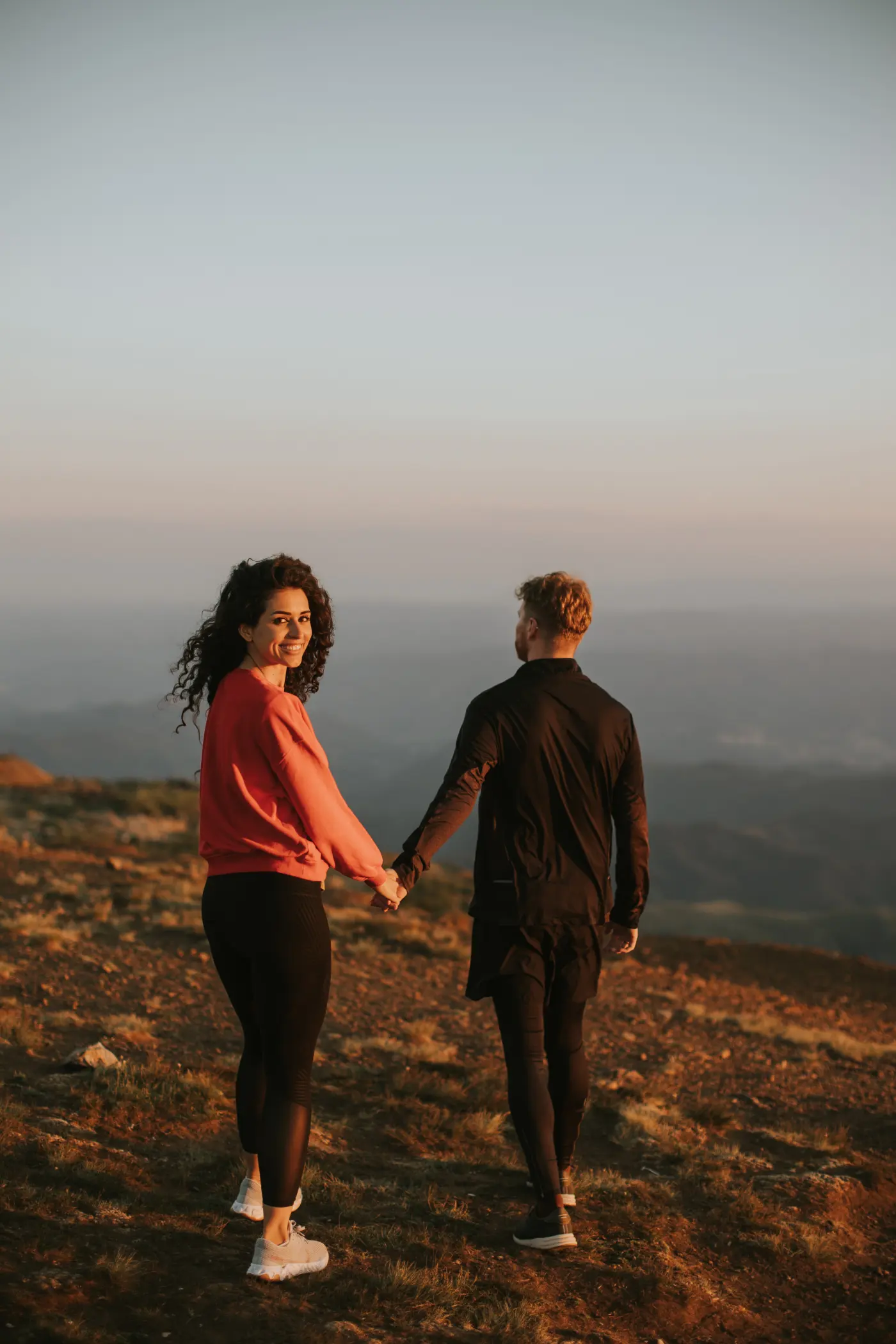 A couple walking hand in hand over green hills at golden hour