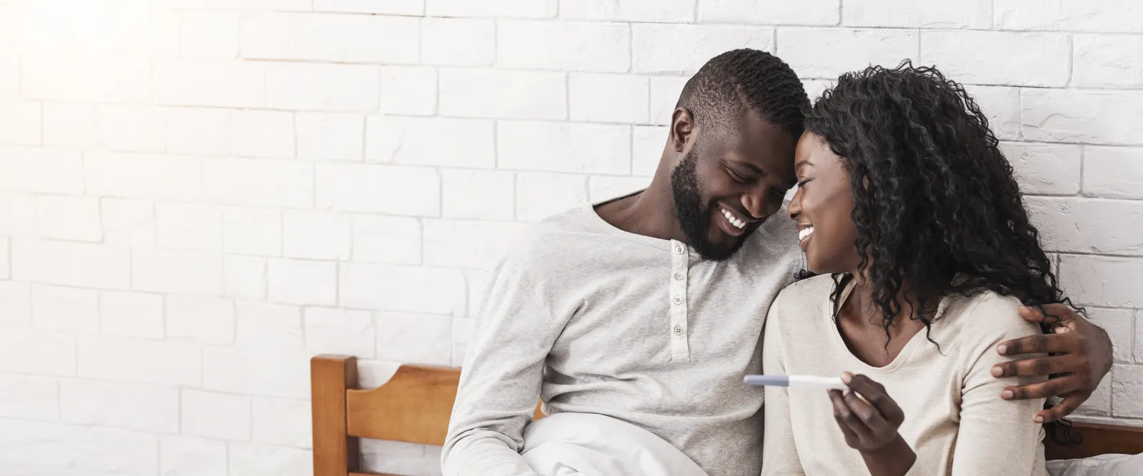 A couple smiling with their foreheads together, holding a positive pregnancy test