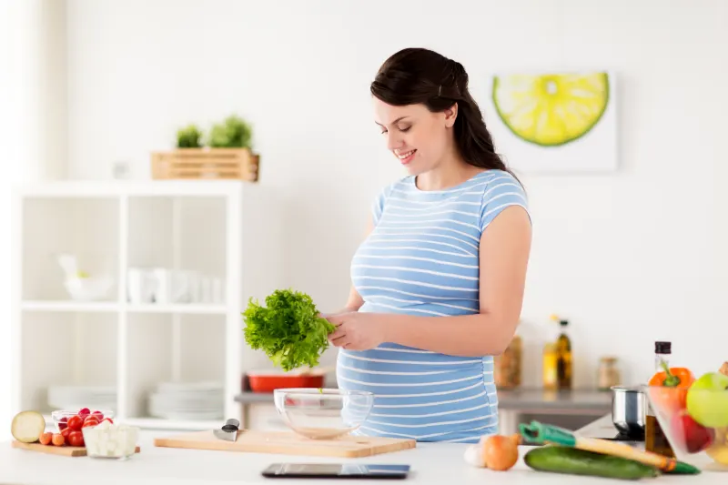 A pregnant woman smiling as she makes a fresh salad at home