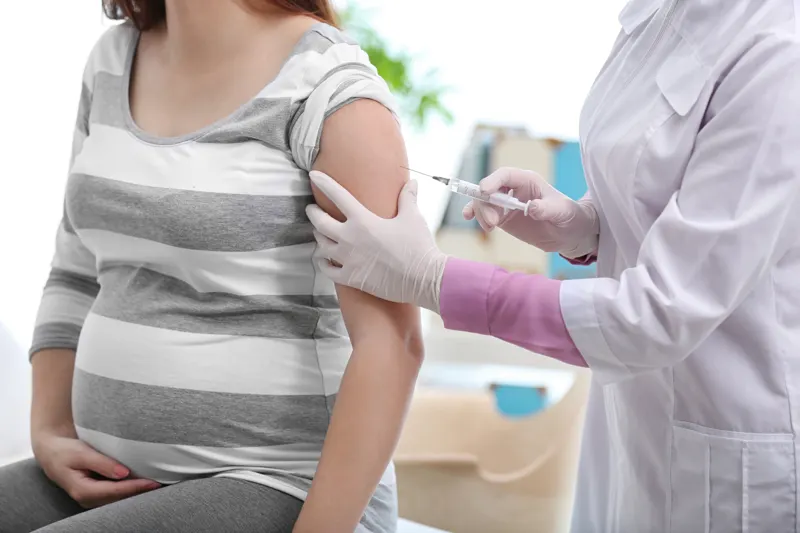 A doctor giving a pregnant woman a vaccine in her upper arm